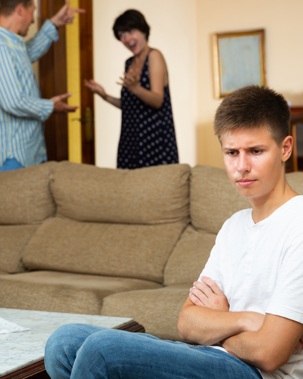 A teen sits with his arms folded with adults in the background